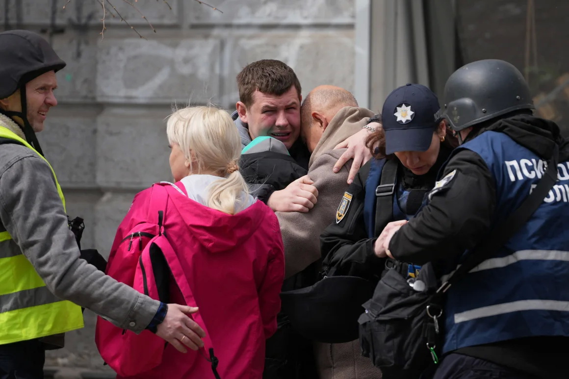 Двоє чоловіків втішають один одного, поки українські поліцейські психологи надають допомогу місцевим жителям. Фото: Олег Вороненко/AFP